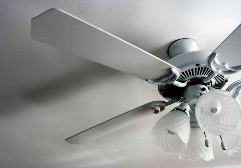 A white ceiling fan in a white room with lights on it.