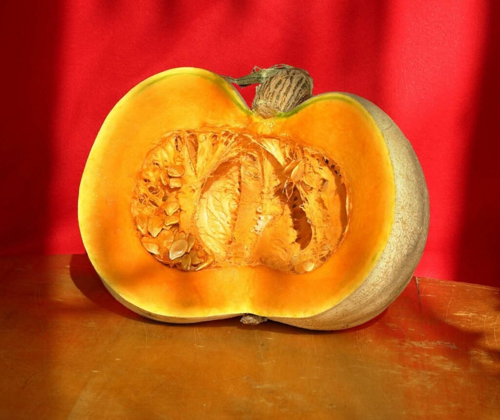 A fresh and big pumpkin cut in half on a wooden table.