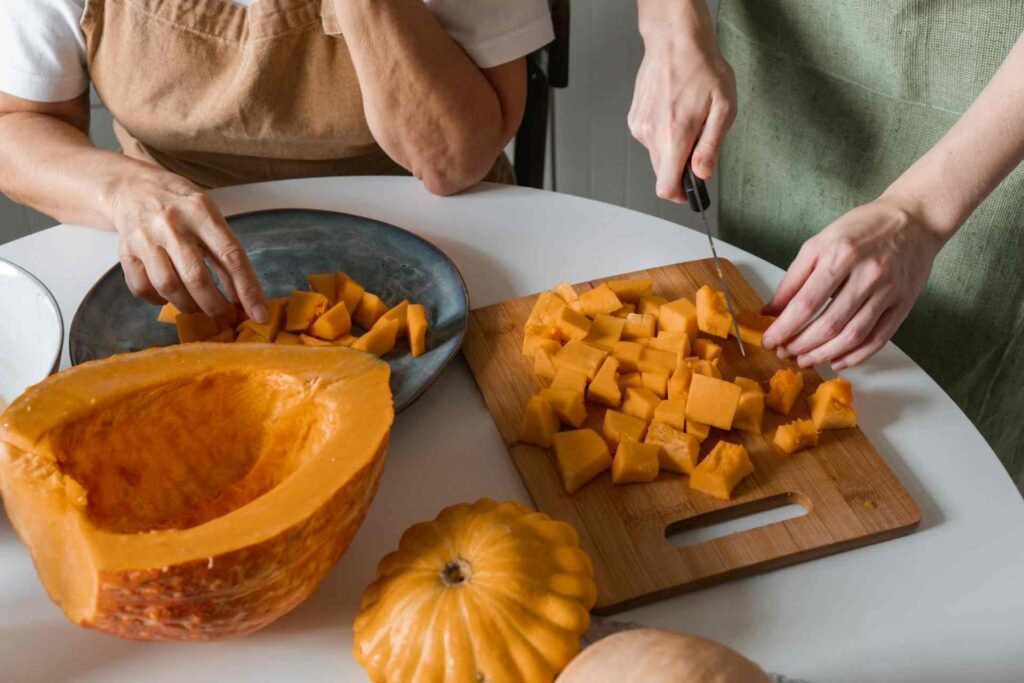 Two people cutting a fresh pumpkin in dices in a kitchen.
