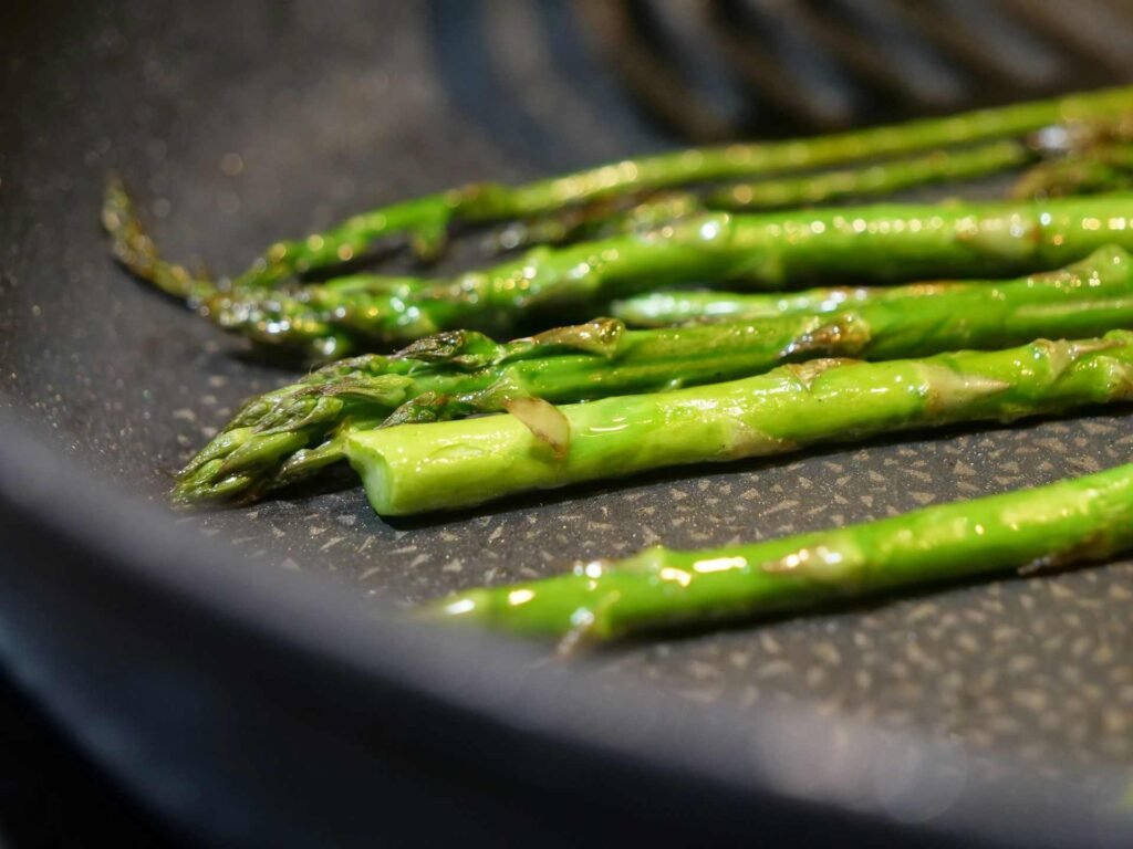 Some green asparagus cooking in a black pan.