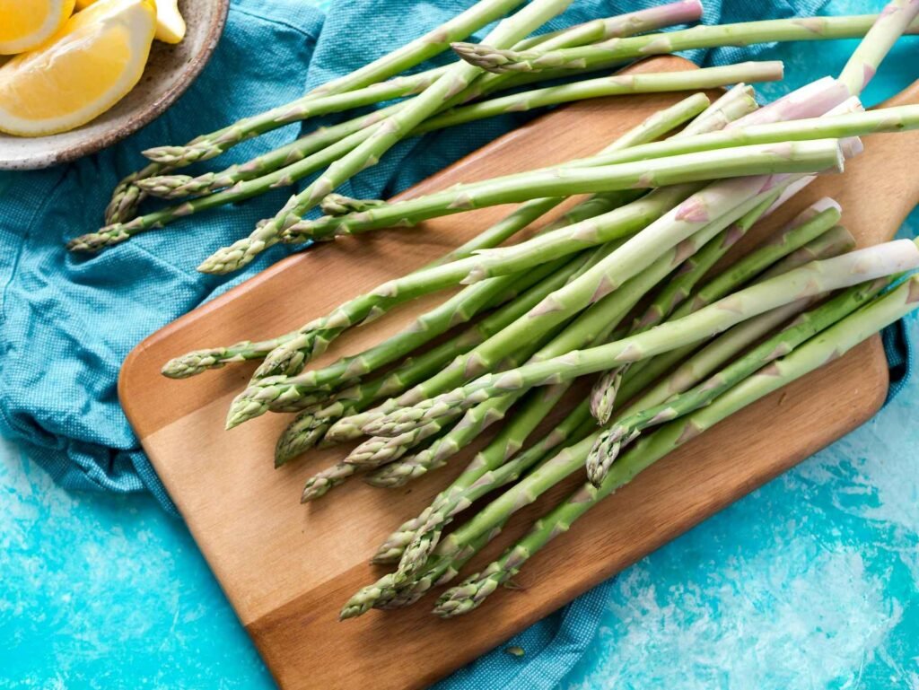 Multiple asparagus spears on a brown chopping board.